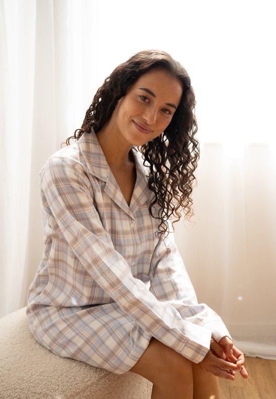 Vrouw met krullend donker haar in een lichtblauw en beige geruit flanellen nachthemd.