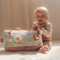 Vrolijke baby zittend naast een activiteitenkussen met bloemen en een hertje.
