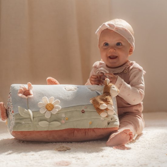 Vrolijke baby zittend naast een activiteitenkussen met bloemen en een hertje.