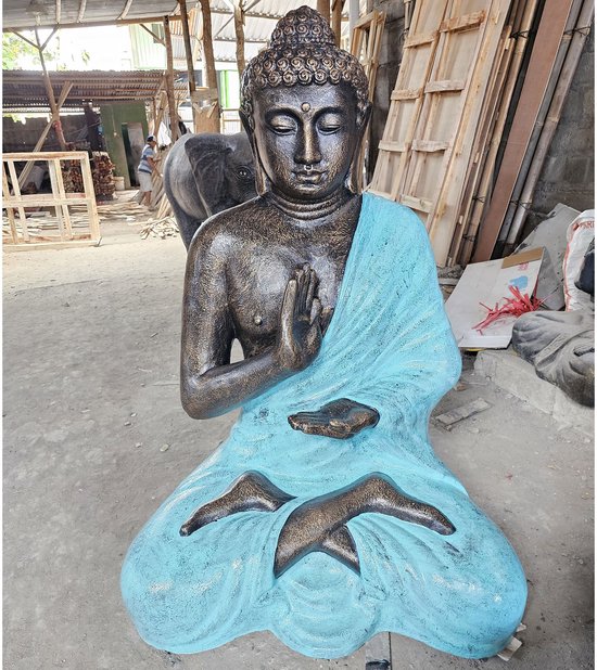 Statue de Bouddha en pierre assise avec robe turquoise, mains en position de prière.