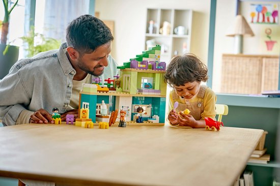 Père et enfant jouant avec une maison Duplo sur une table.