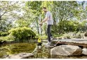 Man plaatst gele Kärcher pomp in een vijver, waterslang is aangesloten.