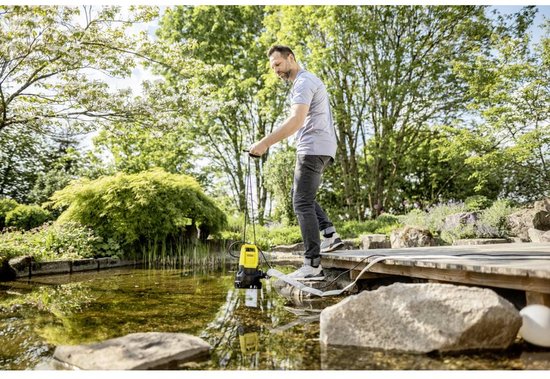 Man plaatst gele Kärcher pomp in een vijver, waterslang is aangesloten.