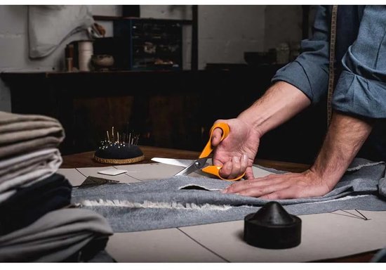 Handen gebruiken oranje Fiskars schaar om grijze stof te knippen.