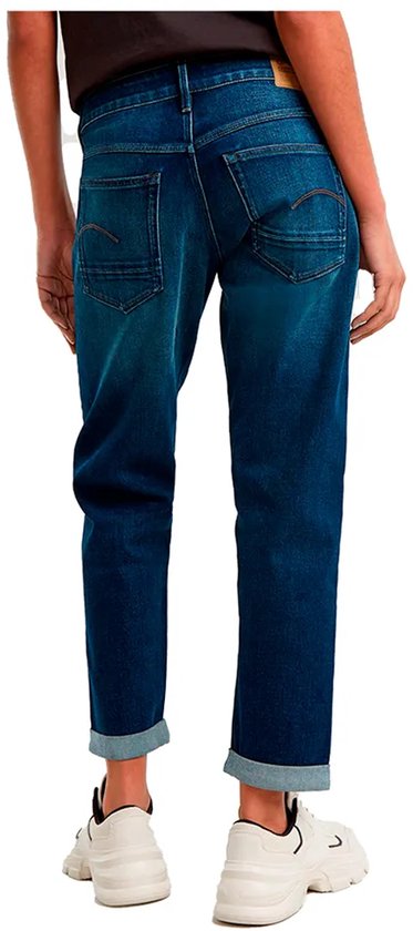 Model draagt een donkerblauwe jeans met omgeslagen broekspijpen, zichtbaar vanaf de achterkant.
