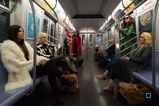 Een groep vrouwen in modekleding, zittend en staand in een metrotrein.