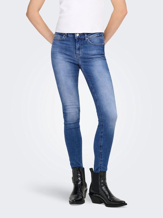 Model draagt een skinny jeans met een lichtblauwe denim wassing en rafelige zoom, gecombineerd met zwarte laarsjes.