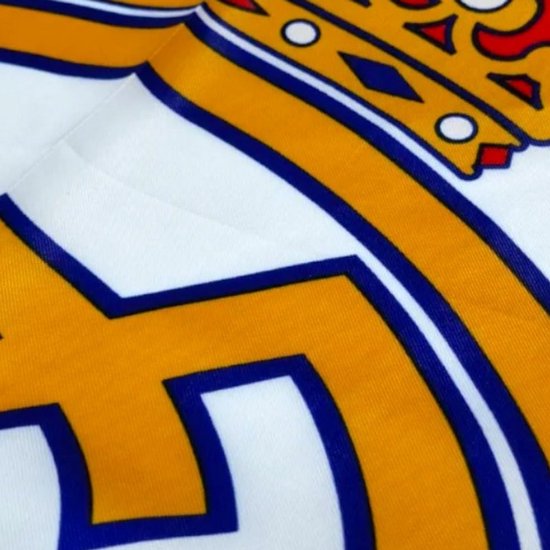 Detail van het Real Madrid logo met gouden kroon op witte achtergrond.