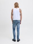 Man met blond haar en tatoeages, draagt een witte tanktop en een lichtblauwe slim fit jeans.