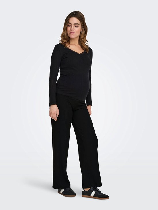 Model van opzij met een zwarte nauwsluitende top en een zwarte wijde ribbroek.