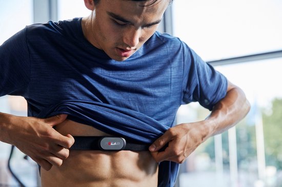 Man met spierbuik draagt een zwarte Polar hartslagsensor op zijn borst, trekt shirt omhoog.