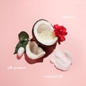 Hibiscusbloem, kokosolie, zijdeproteïne en een klodder crème op een roze achtergrond.