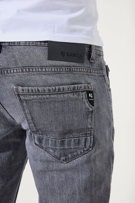 Achterkant van een grijze heren jeans. Met Garcia logo op de achterzak en een zwart leren patch met logo.
