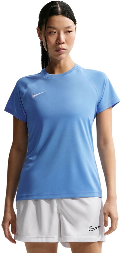 Model in een lichtblauwe Nike sportshirt met korte mouwen en een wit Nike logo. Draagt een witte sportbroek met zwart Nike logo.