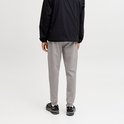 Achterkant van een man in grijze joggingbroek, zwarte jas en zwarte sneakers. Witte achtergrond.