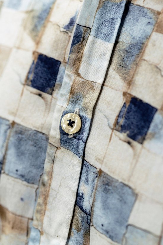 Detailopname van een knoop op een overhemd met een blauw en bruin blokpatroon.
