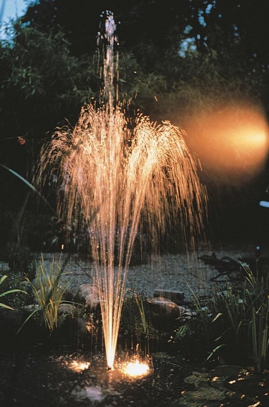 Pompe de fontaine projetant de l'eau dans l'obscurité, illuminée par une lueur chaude.