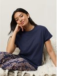 Model zit, draagt een marineblauwe pyjamaset met Schotse hooglanderprint.