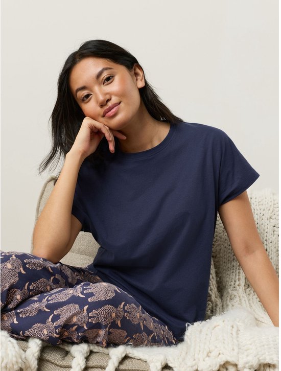 Model zit, draagt een marineblauwe pyjamaset met Schotse hooglanderprint.