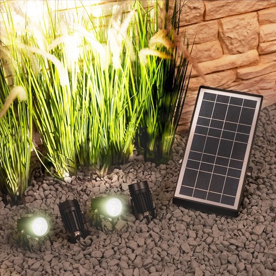 Zwarte prikspots met wit licht, naast een zonnepaneel en wuivend gras.