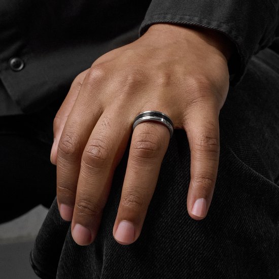 Close-up van een hand met een ring. De ring is zilverkleurig met zwarte details en een gegroefd patroon.