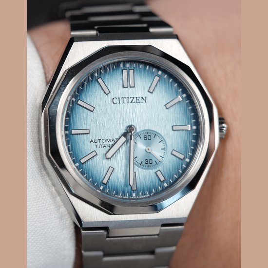 Citizen horloge gedragen op een arm, met een zilverkleurige titanium kast en band. Lichtblauwe wijzerplaat met geborstelde afwerking.