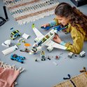 Een jong meisje speelt met een LEGO passagiersvliegtuig, met accessoires zoals een cateringwagen en auto.
