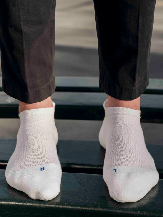 Een close-up van een persoon die witte enkelsokken draagt met een blauwe 'R' op de rechter sok en 'L' op de linker sok.