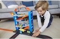 Jongetje speelt met een blauwe Hot Wheels Stunt Garage speelgoedauto garage, gevuld met kleurrijke speelgoedauto's.
