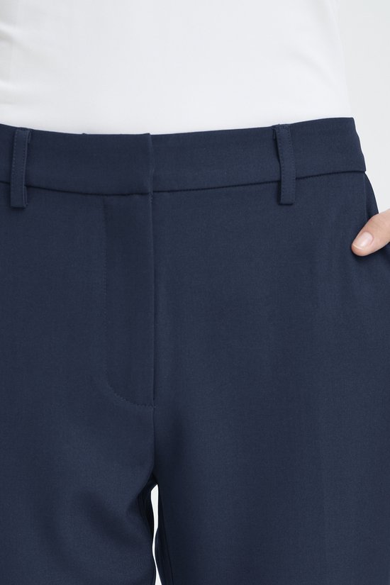 Detail van de tailleband en zak van een donkerblauwe broek.