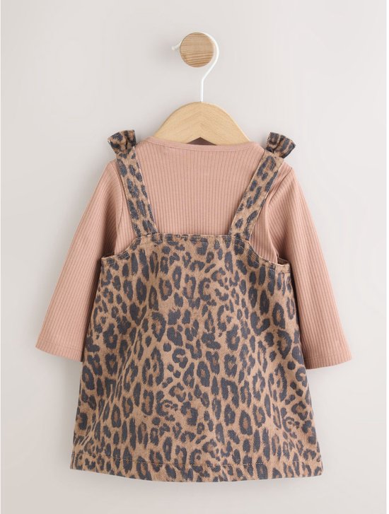 Roze ribgebreide romper met luipaardprint denim jurkje met strikbandjes op de schouders, hangend aan een kledinghanger.