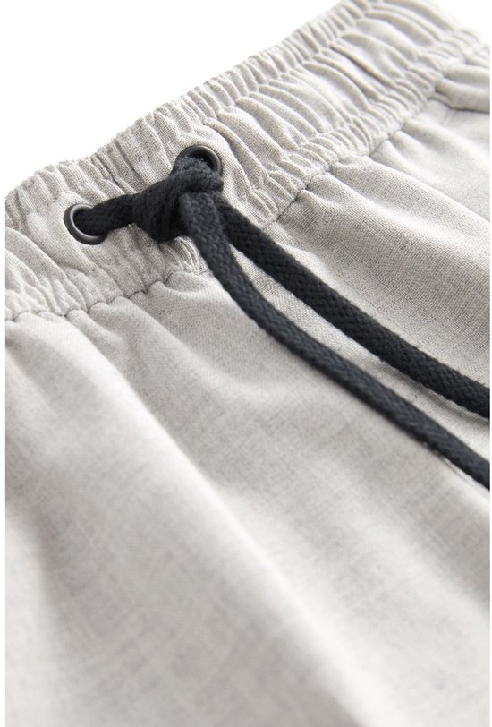 Close-up van de elastische tailleband van een lichtgrijze pantalon met zwart trekkoord.