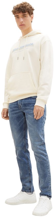 Man in een crème hoodie met opdruk en blauwe slim fit jeans.