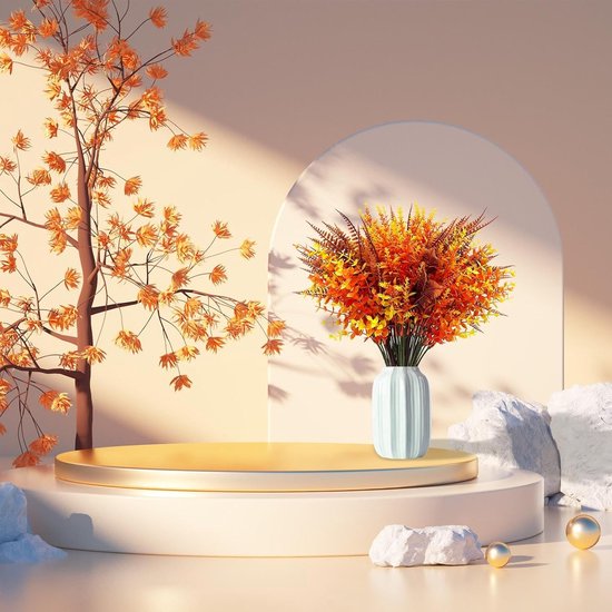 Plantes artificielles orange, jaune et brun rouille dans un vase blanc sur une plateforme dorée.
