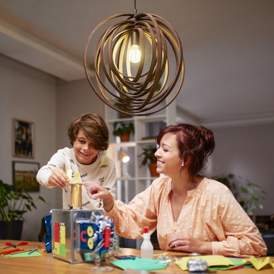 Moeder en zoon knutselen aan een robot onder een moderne hanglamp.