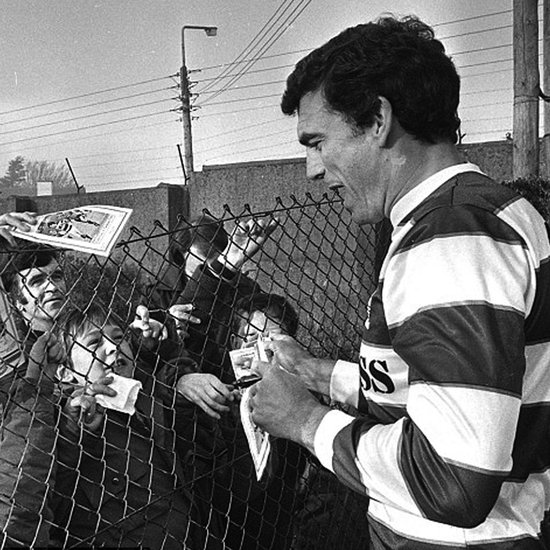 Zwart-witfoto van een man in gestreept voetbalshirt, die handtekeningen uitdeelt aan fans.