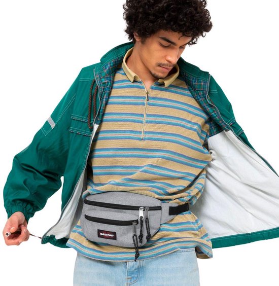 Sac banane Eastpak gris avec logo, porté par un homme portant un pull à rayures et une veste verte.
