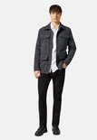 Model in een grijze jas met vier zakken, wit overhemd en zwarte jeans.