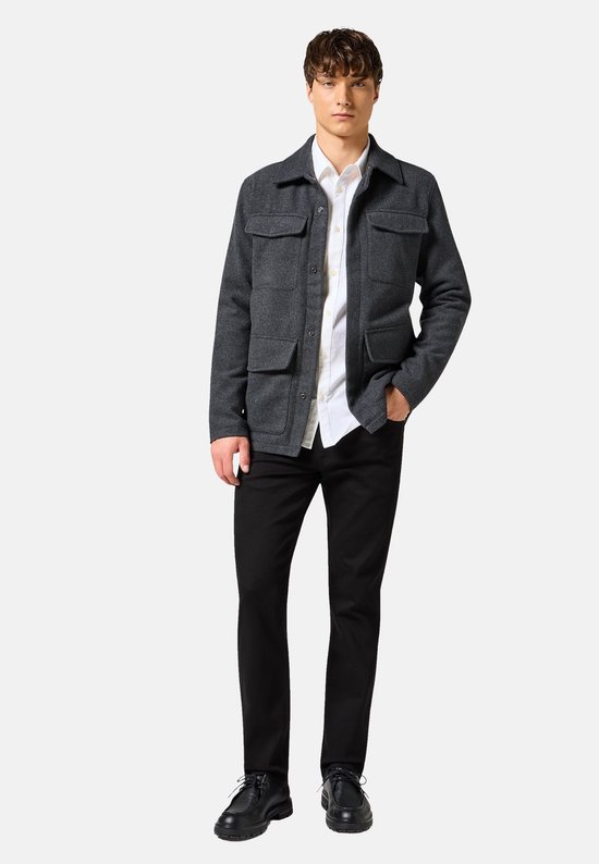 Model in een grijze jas met vier zakken, wit overhemd en zwarte jeans.