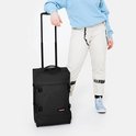 Persoon in lichtblauwe trui en spijkerbroek met een zwarte Eastpak koffer.
