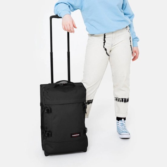 Persoon in lichtblauwe trui en spijkerbroek met een zwarte Eastpak koffer.