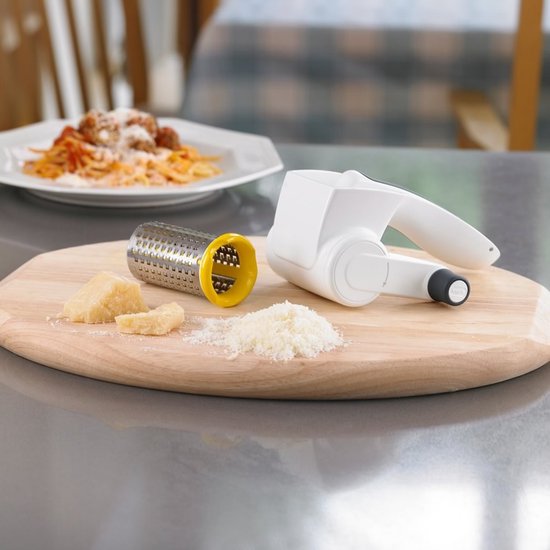 Kaasrasp met witte handgreep, zilveren trommel en gele opening, naast geraspte kaas, een stuk kaas en een bord spaghetti.