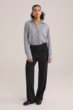 Model draagt een zwarte jersey broek met regular fit en wijde pijpen, met een gestreepte blouse en sneakers.