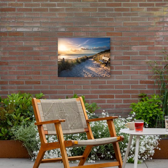Canvasprint van een zonnig strandpad met duinen, gras en een houten bankje, gezien vanaf een tuin met stoel.