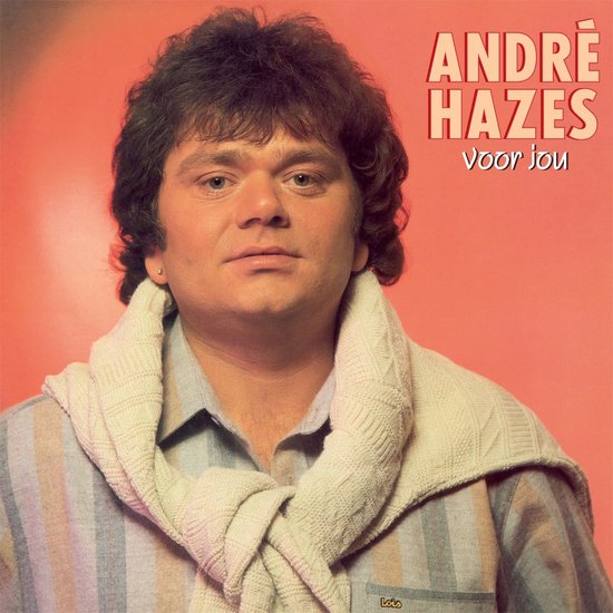 André Hazes draagt een gestreepte blouse met een gebreide sjaal om zijn nek, tegen een oranje achtergrond. "ANDRÉ HAZES voor jou" staat in de rechterbovenhoek.
