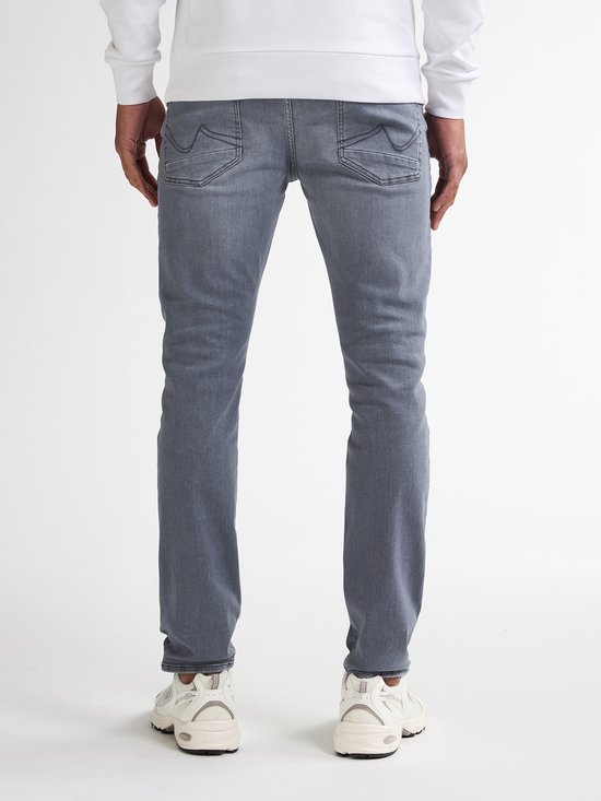 Achterkant van een man die een grijze slim fit jeans en witte sneakers draagt.