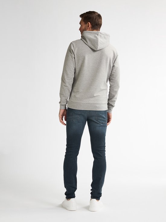 Man van achteren gezien, draagt een grijze hoodie en blauwe slim fit jeans. Witte sneakers.