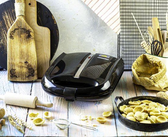 Gesloten zwarte koekjesmaker met nootjesvorm, omringd door kookgerei en ingrediënten.