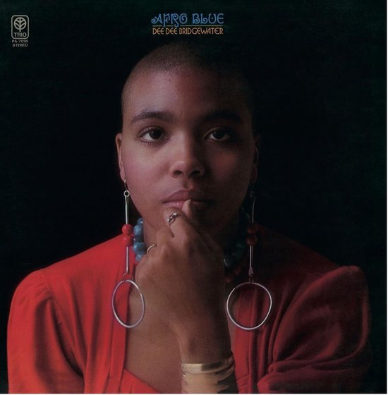 Dee Dee Bridgewater met korte coupe, draagt rode jurk en grote oorbellen met kralen.