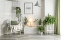 Lichtgroene gordijnen in een woonkamer met veel planten en een mandenstoel.